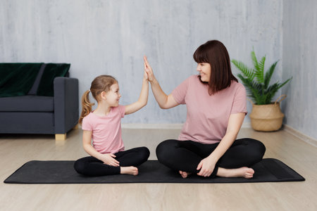 family and sport concept - young mother and little girl doing sport exercises together and clapping hands at homeの写真素材