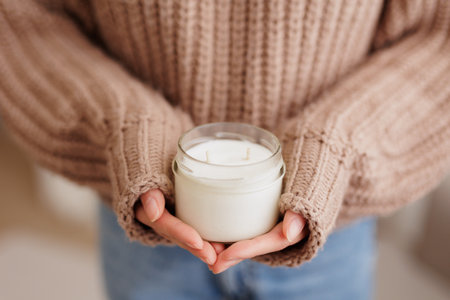 Woman in brown sweater holding finished  white candle in handsの写真素材