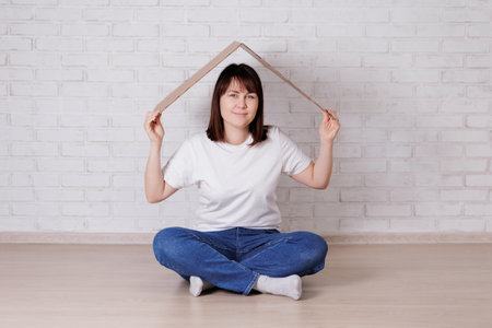 Happy woman sitting under cardboard roof on the floorの写真素材