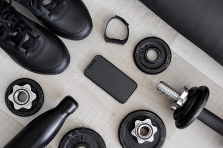 Flat lay of mobile phone and black sport equipment on wooden background