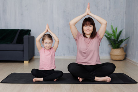 young mother and little daughter doing yoga together in living room at homeの写真素材