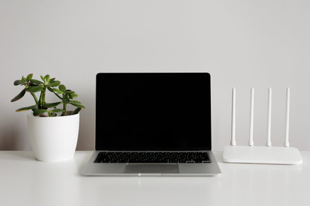 Open laptop, router and green plant on white tableの写真素材