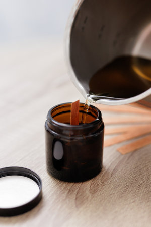 Yellow liquid pouring wax from pan into dark glass bottle formの写真素材