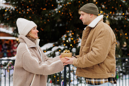 Young man giving gift to his happy girlfriend near christmas treeの写真素材