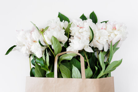 Beautiful white peonies and leaves in brown paper bagの写真素材