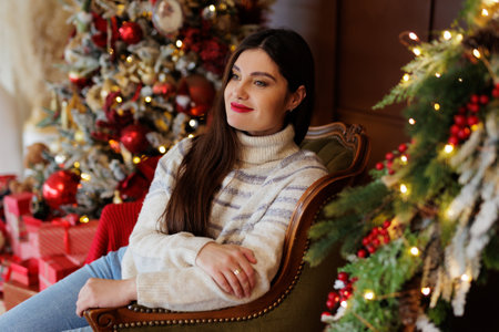 Portrait of dreaming woman in sweater near christmas tree with lights and giftsの写真素材