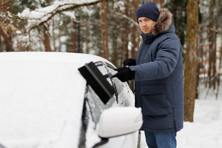 young man cleaning his car with brush after a snowfall