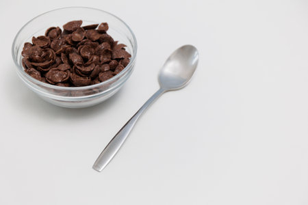 Chocolate cereals served in glass bowl with spoon on white background with copy spaceの写真素材