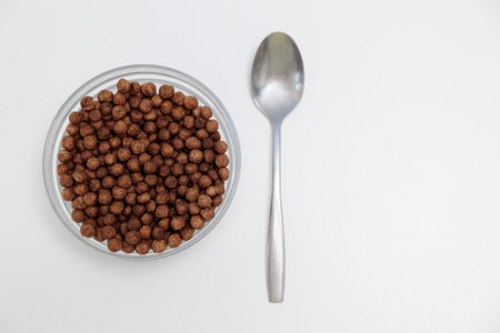 Top view of crunchy chocolate breakfast balls in glass bowl with spoon on white with copyspace