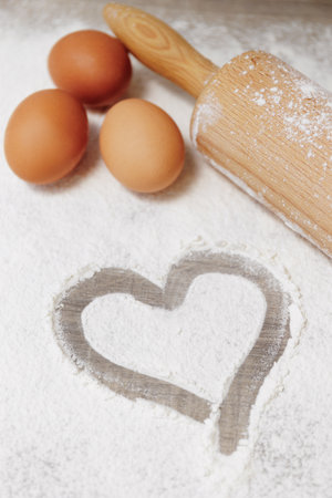 Top view of rolling pin,eggs and heart shape made with flour on wooden backgroundの写真素材