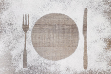 Top view of plate, spoon and fork silhouette made with flour on wooden backgroundの写真素材
