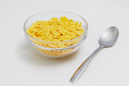 Golden corn flakes served in glass bowl with spoon on white