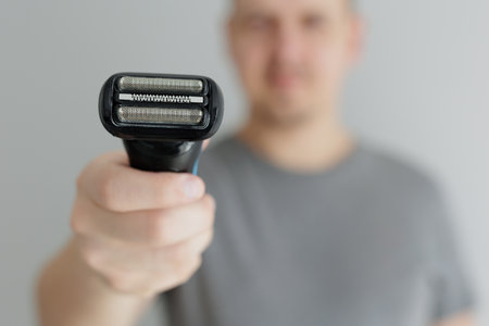Close up of black electric razor in male hands in grey tshirt