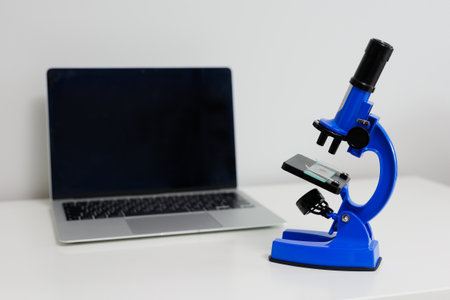 Computer and blue microscope on white table with copyspace