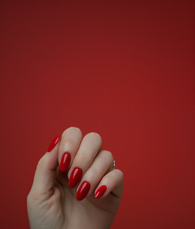 Close up of female hand with red manicure on red background with copy spaceの素材