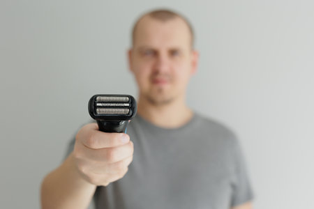 Close up of electric razor in male hands in grey tshirt