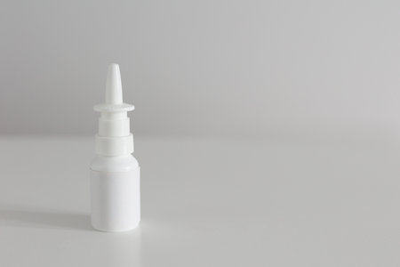 A white bottle without a label for a nasal spray stands vertically on a white table with copyspaceの写真素材
