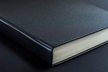 close up of black closed book with blank cover over black table backgroundの素材