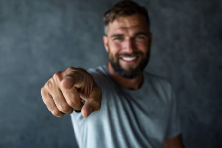 handsome muscular man in sporty clothes pointing forward to camera over grey studio backgroundの素材