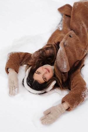 a woman in brown coat lies on white snowの写真素材
