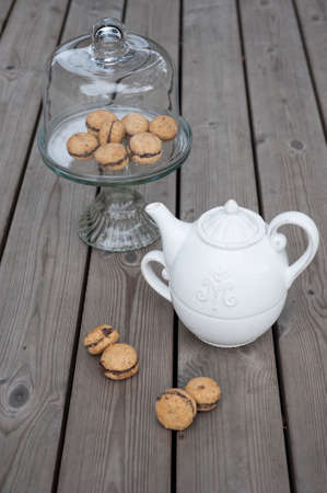 Lady's Kisses - Italian hazelnut sandwich cookies on cake stand with White ceramic teapotの写真素材