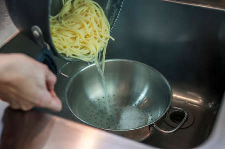 pot with spaghetti during the operation of the water draining cooking salt in the kitchen sinkの写真素材