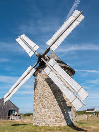 An old windmill on the coast of Normandy. Stone structure, wooden gears and bare white coated blades