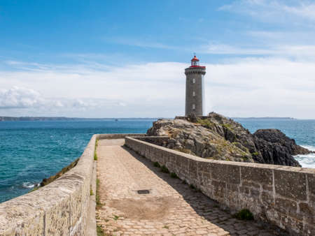 Ancient stone pier with lighthouse on the rocks overlooking the oceanの写真素材