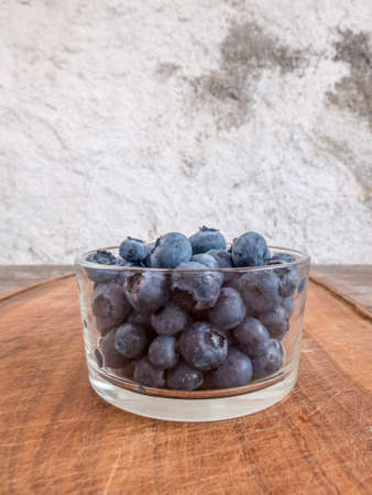 Blueberries in glass cup on wooden cutting boardの写真素材