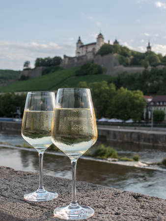 pair of white wine glasses on stone wall with landscape in the background of a Wurzburg wine estate and its vineyards in the northern Bavaria region, Germany.の写真素材