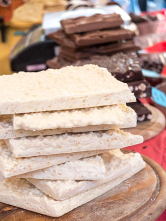 pieces of crude white chocolate stacked on wooden chopping boards. In the background other pieces of mixed chocolate. Red tablecloth in the background.の写真素材