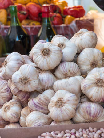 pile of garlic heads of Vessalico exposed at a banquet of the market. In the background wine bottles and yellow and red peppers in the exhibition.の写真素材