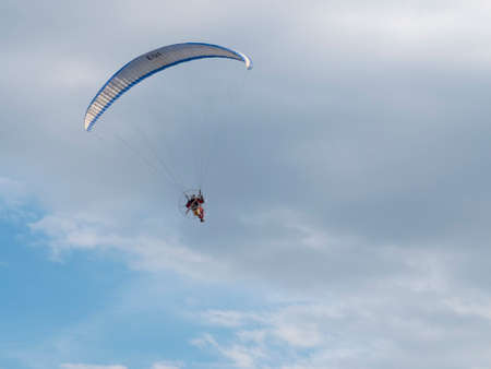 man on motorized hang glider taken from the ground on cloudy skyの写真素材