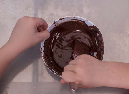 hands of a child play the pastry chef mixing chocolate in a bowl before pouring it into the chocolates molds. View from above.の写真素材