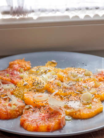 Gray plate, orange and onion salad. Leaning on a wooden table, seen from above.の写真素材