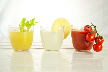 Three glasses with 3 different juices: tomato, pineapple and celery