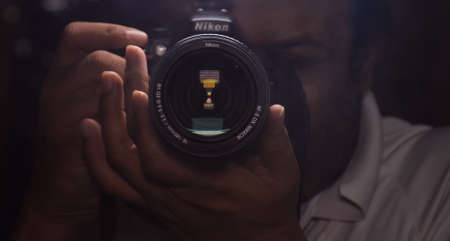 Male photographer clicking picture with his DSLR Camera. Photographer is blurred on dark backgroundの写真素材