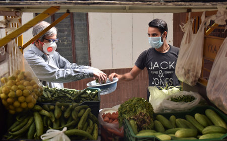 An Indian customer and vegetable seller maintaining social distancing and wearing face mask while buying and selling vegetables as a precaution against covid 19のeditorial素材