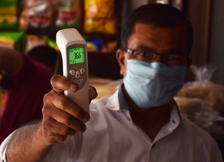 An Indian showing his  Non-Contact Laser IR Temperature Gun or Thermal Scanner which is used to measure body temperature of a person. Digital Thermometer Gunのeditorial素材