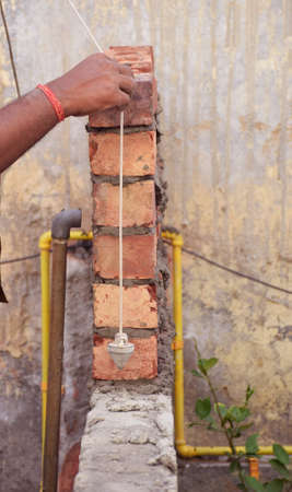 Indian professional construction worker measuring brick wall for accurate proportion with his tool.の写真素材
