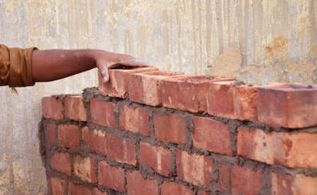 An Indian professional construction worker laying bricks during construction of a wall. Details of...