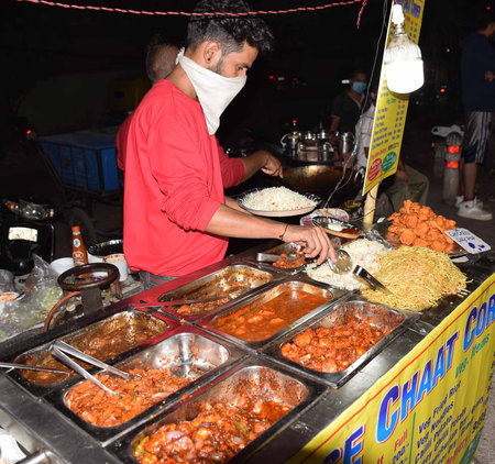 An Indian street vendors selling Chinese food is serving noodles to his customerのeditorial素材