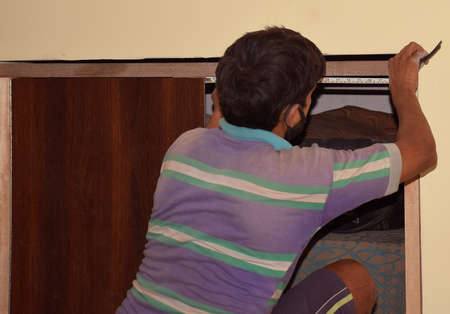 An Indian carpenter measuring a wooden frame for correct adjustment to fit inside the wallの写真素材