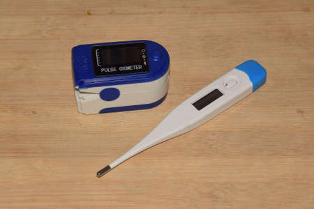 Pulse Oximeter and digital thermometer kept on a wooden surfaceの写真素材