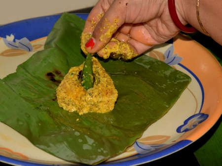 Bengali women preparing Ilish paturi dish where fish is smeared with mustard oil and poppy seeds before covering it with banana leaf and then kept it over steamの写真素材
