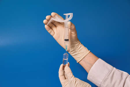 Gloved hand holding syringe on blue backgroundの写真素材