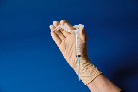 Gloved hand holding syringe on blue backgroundの写真素材