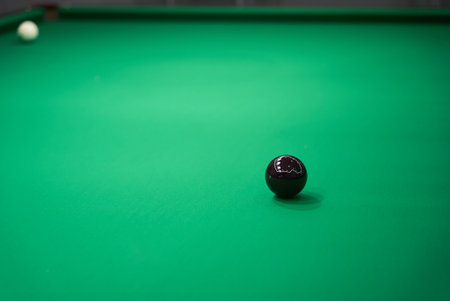 A Detailed CloseUp View of a Black Ball Resting on a Luxurious Green Billiard Tableの写真素材