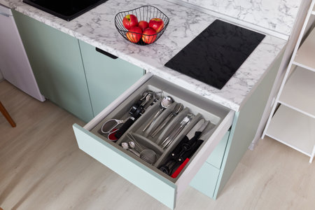 This is a modern kitchen drawer that contains cutlery alongside fresh, vibrant applesの写真素材