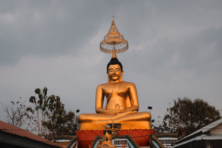 Majestic Golden Buddha Statue Situated Beneath a Dramatic Cloudy Sky Displaying Beautyの写真素材